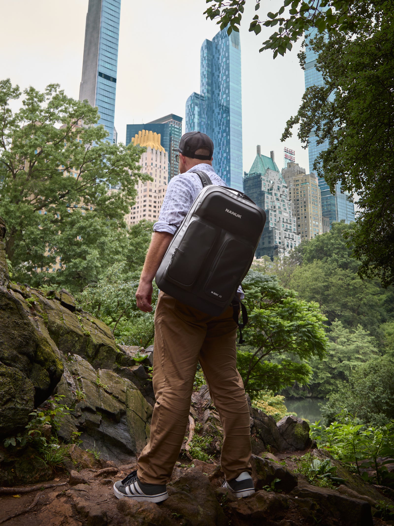 Person mit einem Koffer, die auf einem Felsvorsprung steht, mit der Skyline der Stadt im Hintergrund