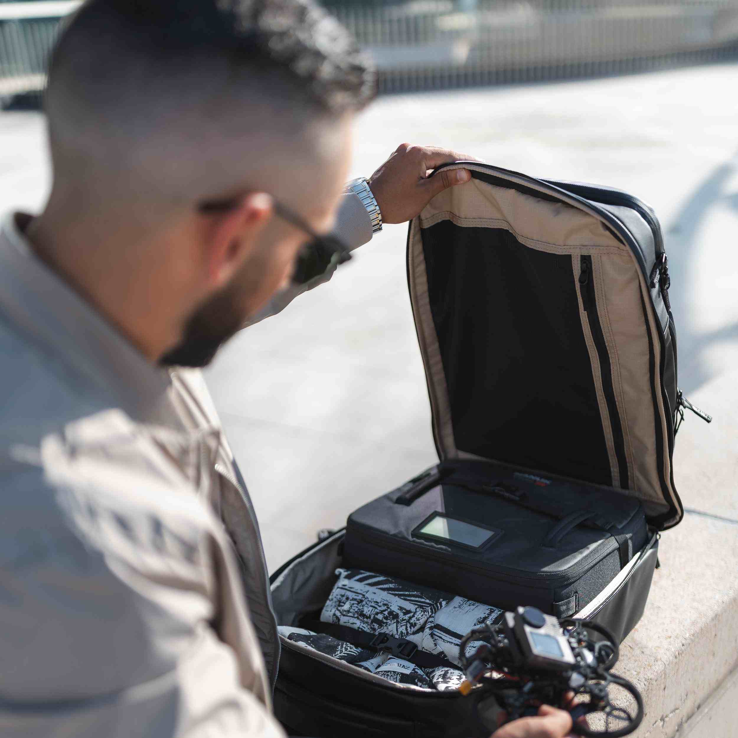 Mann öffnet einen Koffer auf einem Bürgersteig, in dem sich elektronische Geräte befinden. Mann öffnet einen Koffer auf einem Bürgersteig, in dem sich elektronische Geräte befinden.