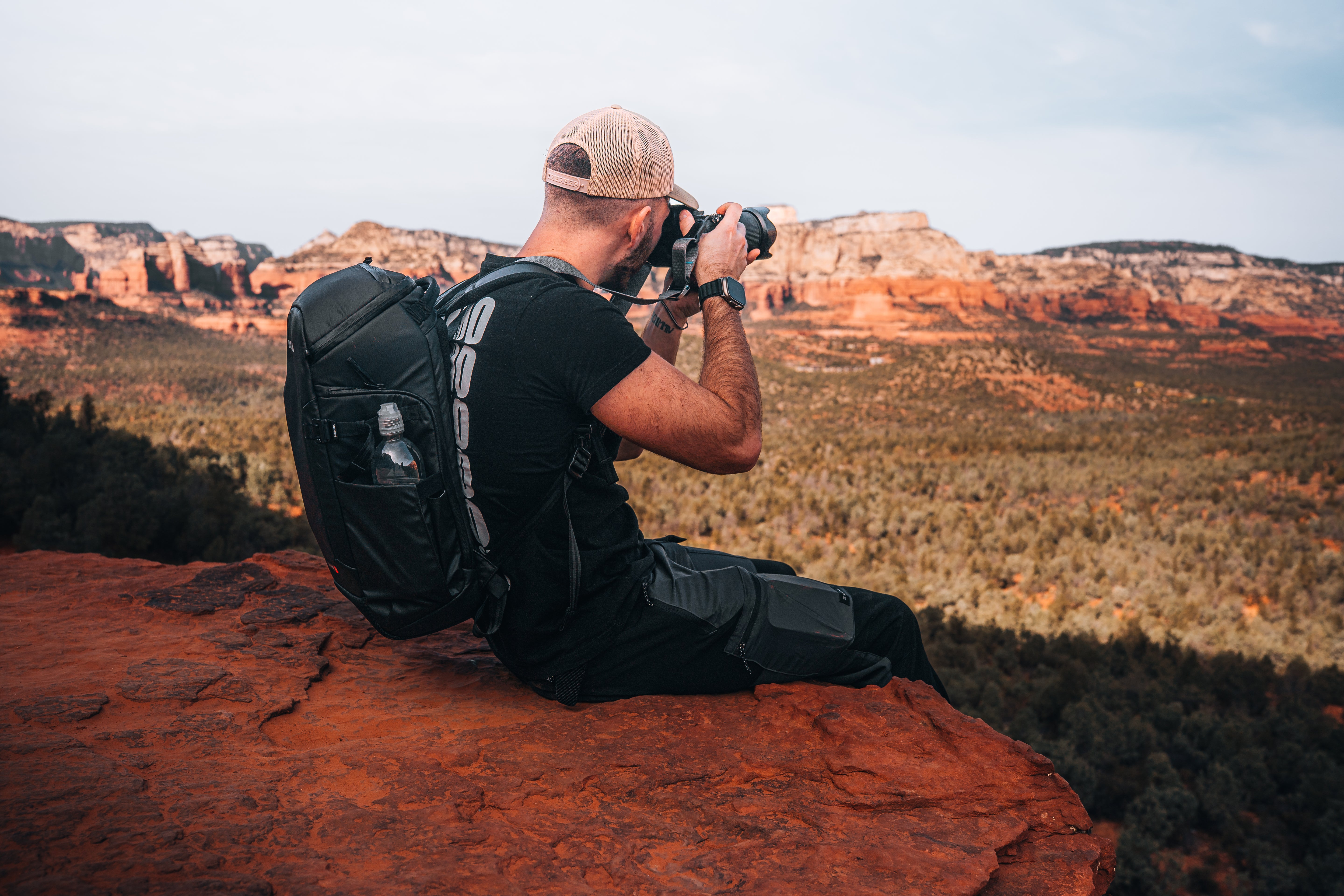Man with a backpack taking a photograph of a scenic landscape.