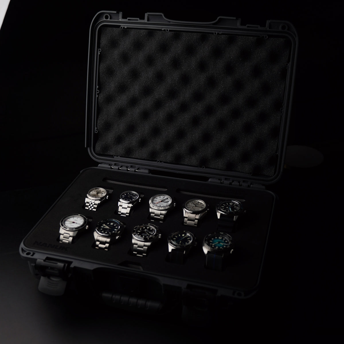 An open black hard watch case with foam insert, holding ten wristwatches on a dark background.