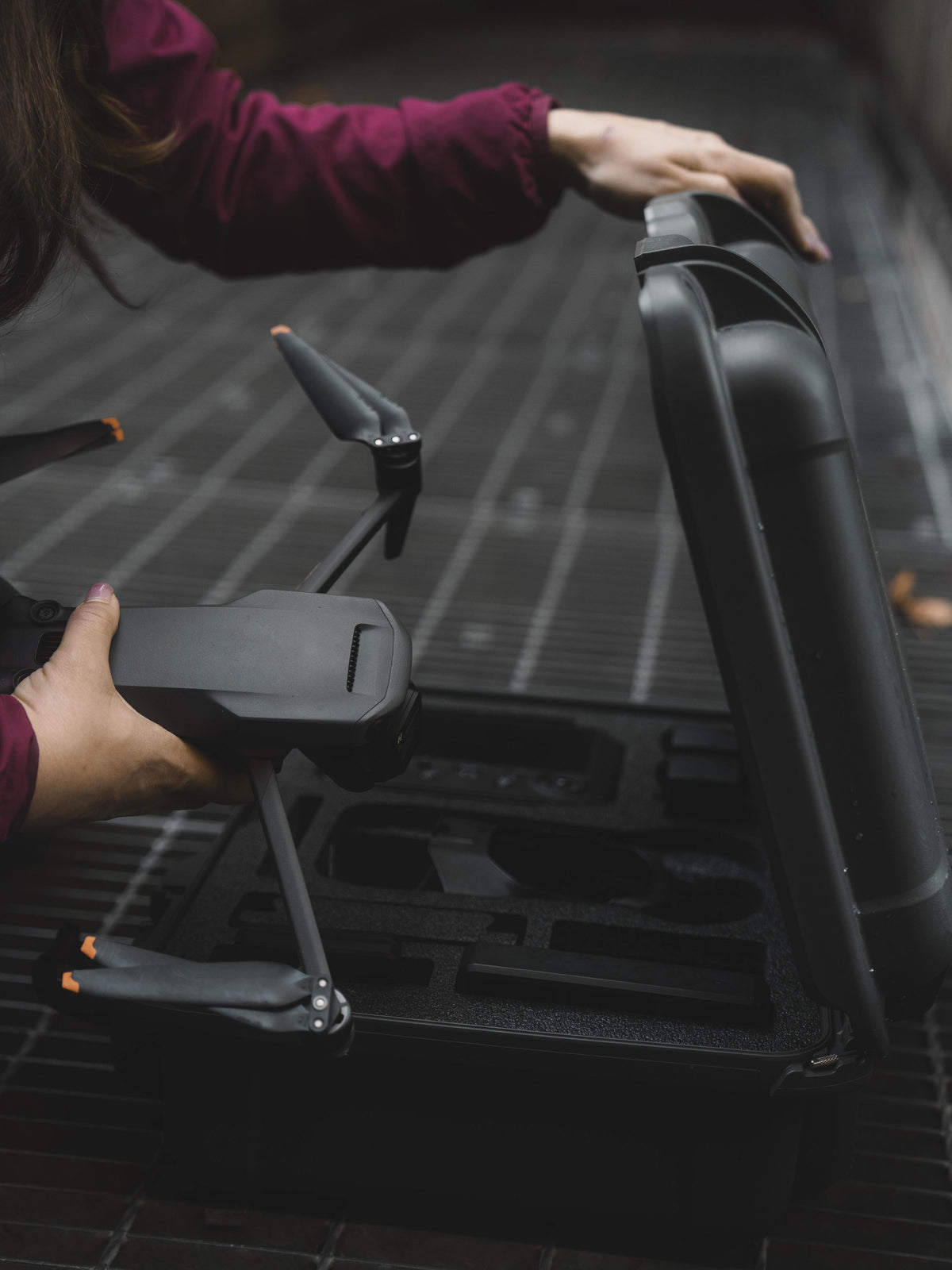 A close-up lifestyle shot of a person's hands placing a black drone into a custom foam-lined hard carrying case, with the case lid propped open.