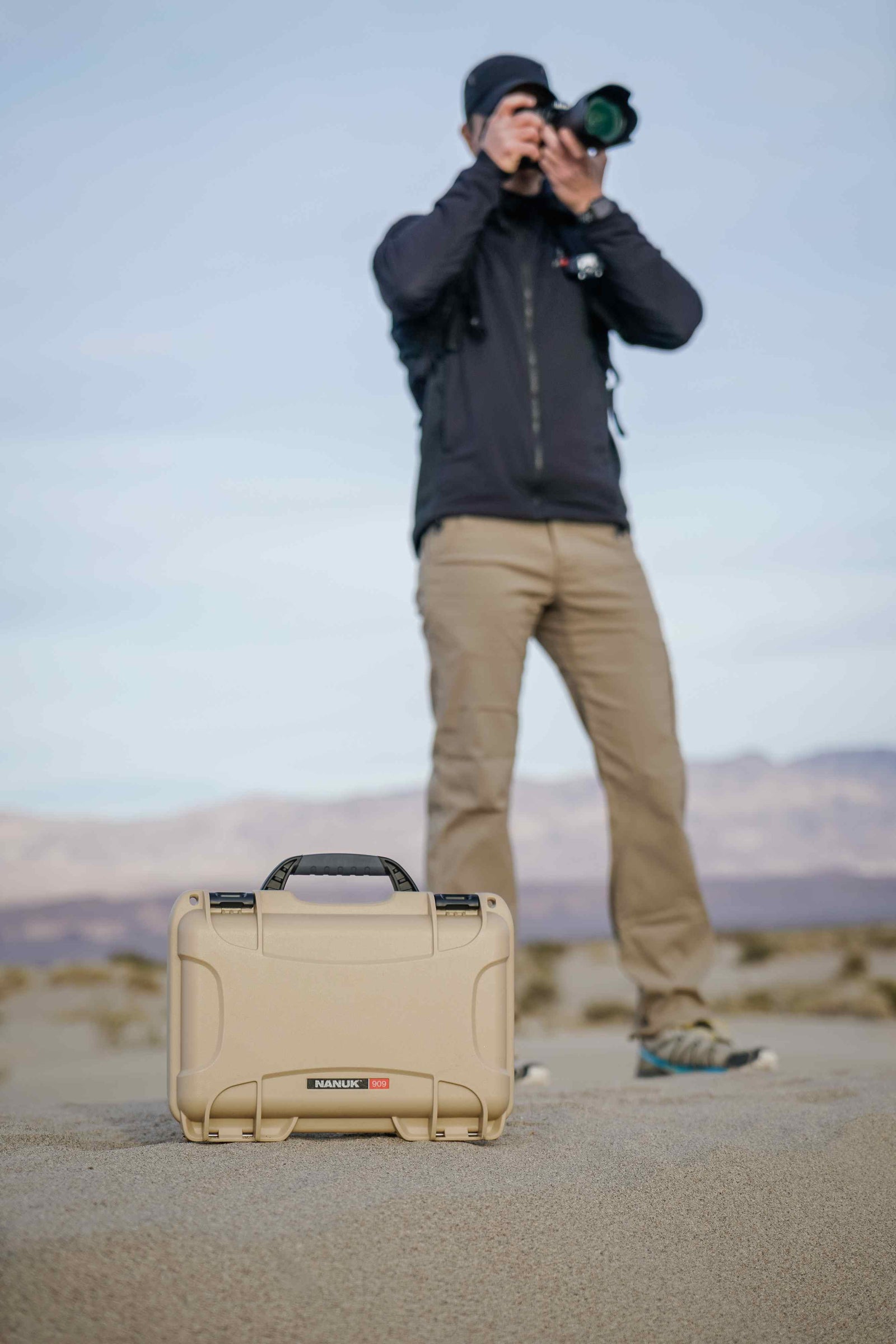 NANUK 909 valise in strapazierfähiger hellbrauner Farbe, der auf Wüstensand unter einem sanften Himmel ruht.