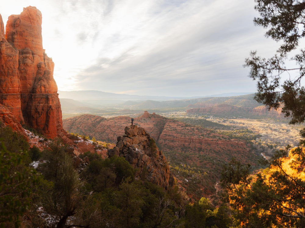 Scenic view of red rock formations and a valley with a person standing on a rocky outcrop.
