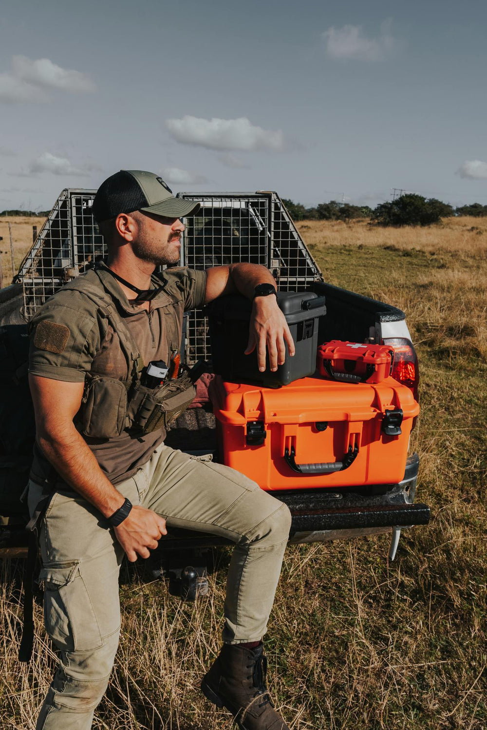 Man sitting on a truck bed with an orange cooler in a field