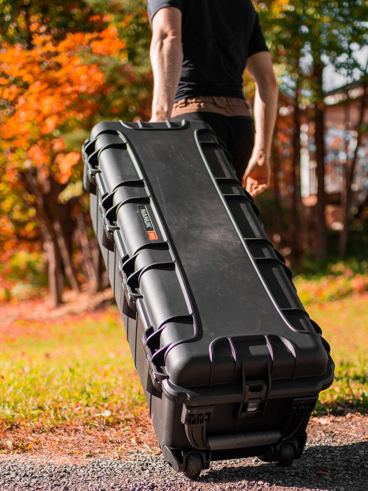 Une personne se trouvant à l'extérieur, dans un parc en automne, tire une grande valise à roulettes noire à coque rigide de la marque « valise ». Cette valise « valise » porte le logo «Zennit» et est équipée de loquets.