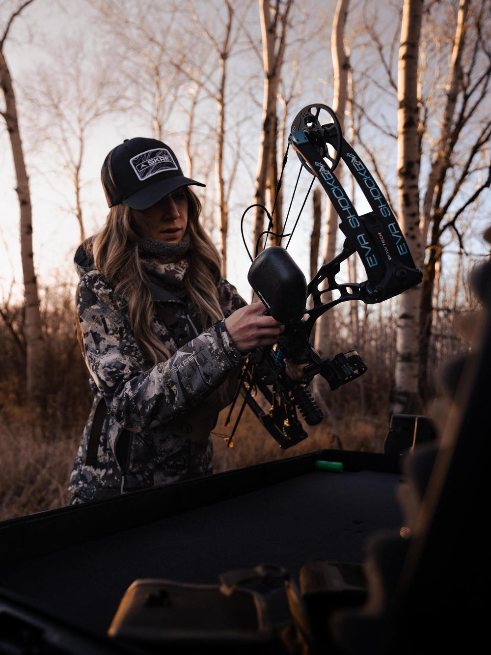 Person in camouflage outfit and cap handling a bow and arrow in a forest setting