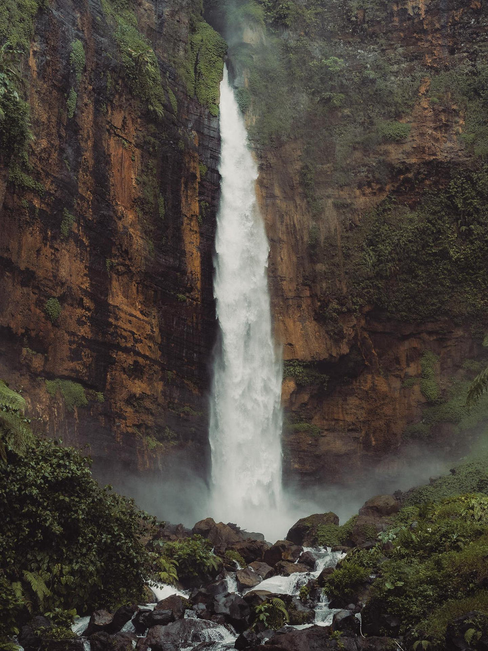 Tall waterfall cascading down a rocky cliff in a lush green forest