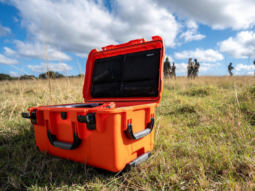 Orange hard-shell case in a grassy field with people in the background