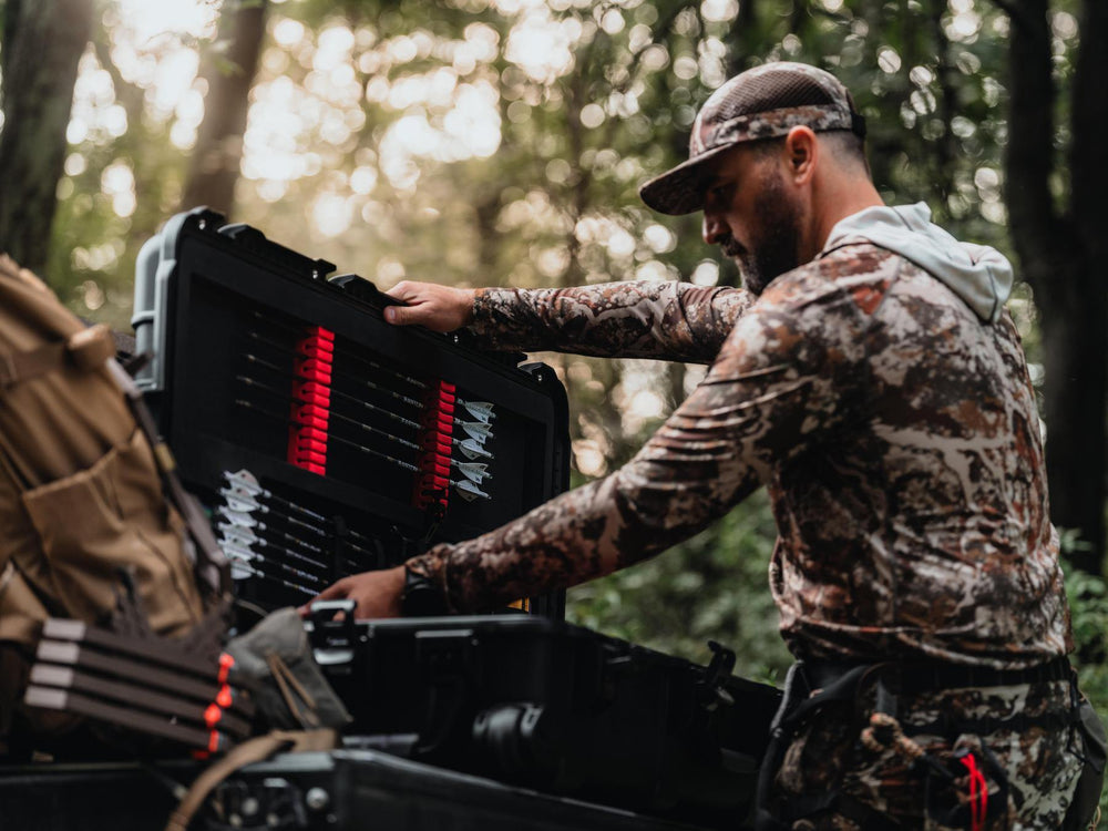 Man in camouflage gear organizing ammunition in a wooded area