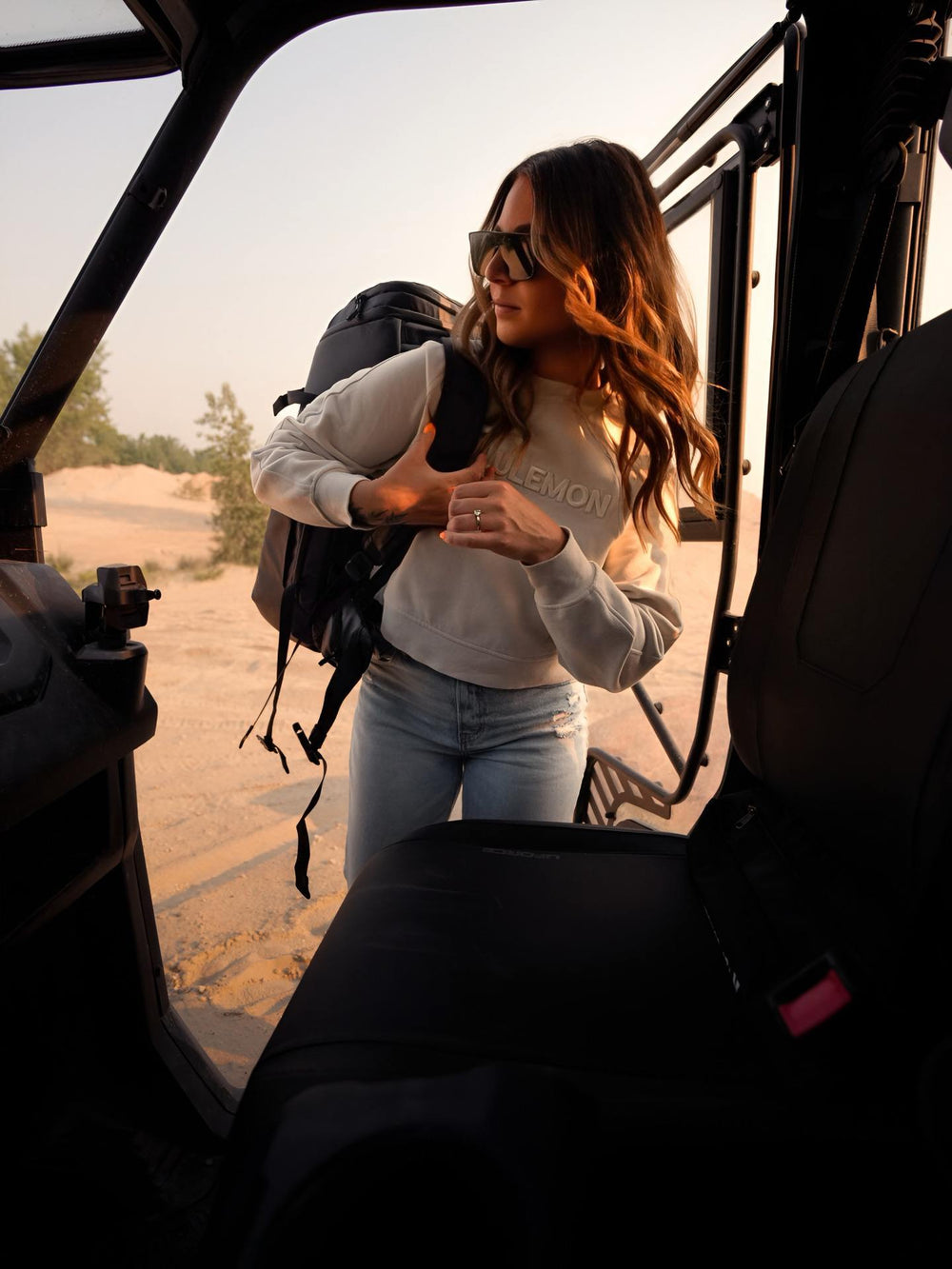 Woman with a backpack standing inside a vehicle in a desert setting