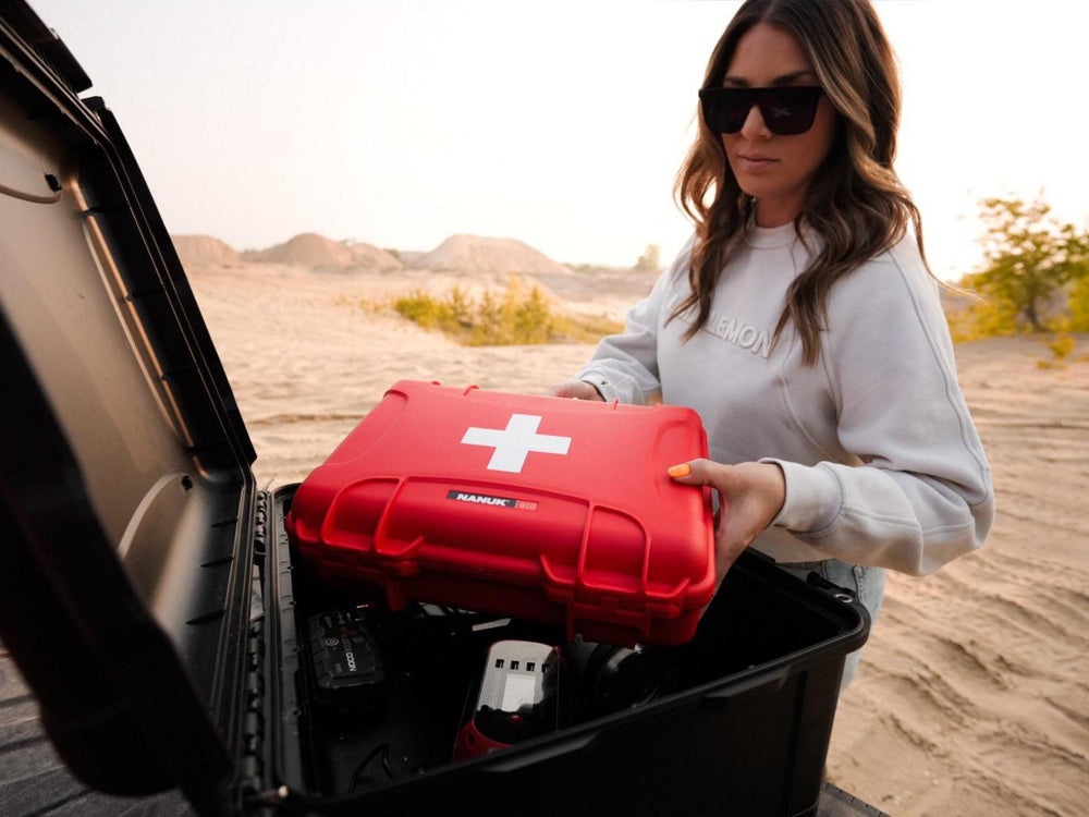 Person holding a red first aid kit in a car trunk with a desert landscape in the background