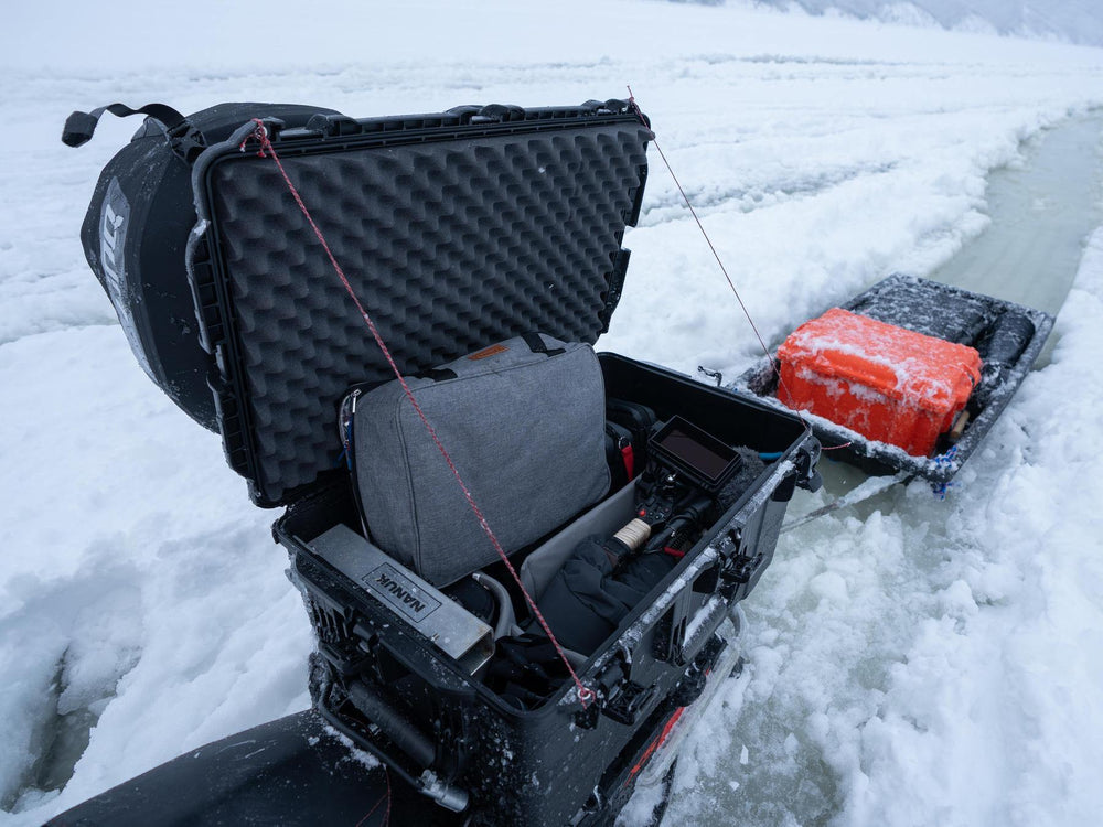 Ice fishing setup with a black fishing chair, rod, and red cooler on a frozen lake.
