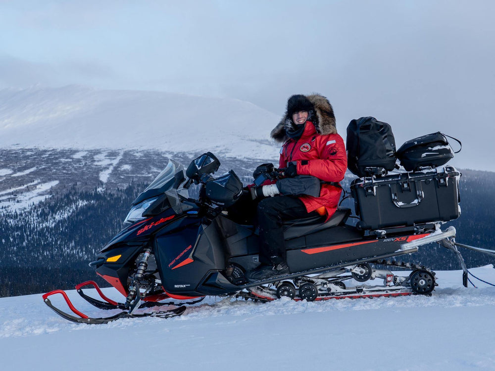 Person sitting on a snowmobile in a snowy landscape with mountains in the background