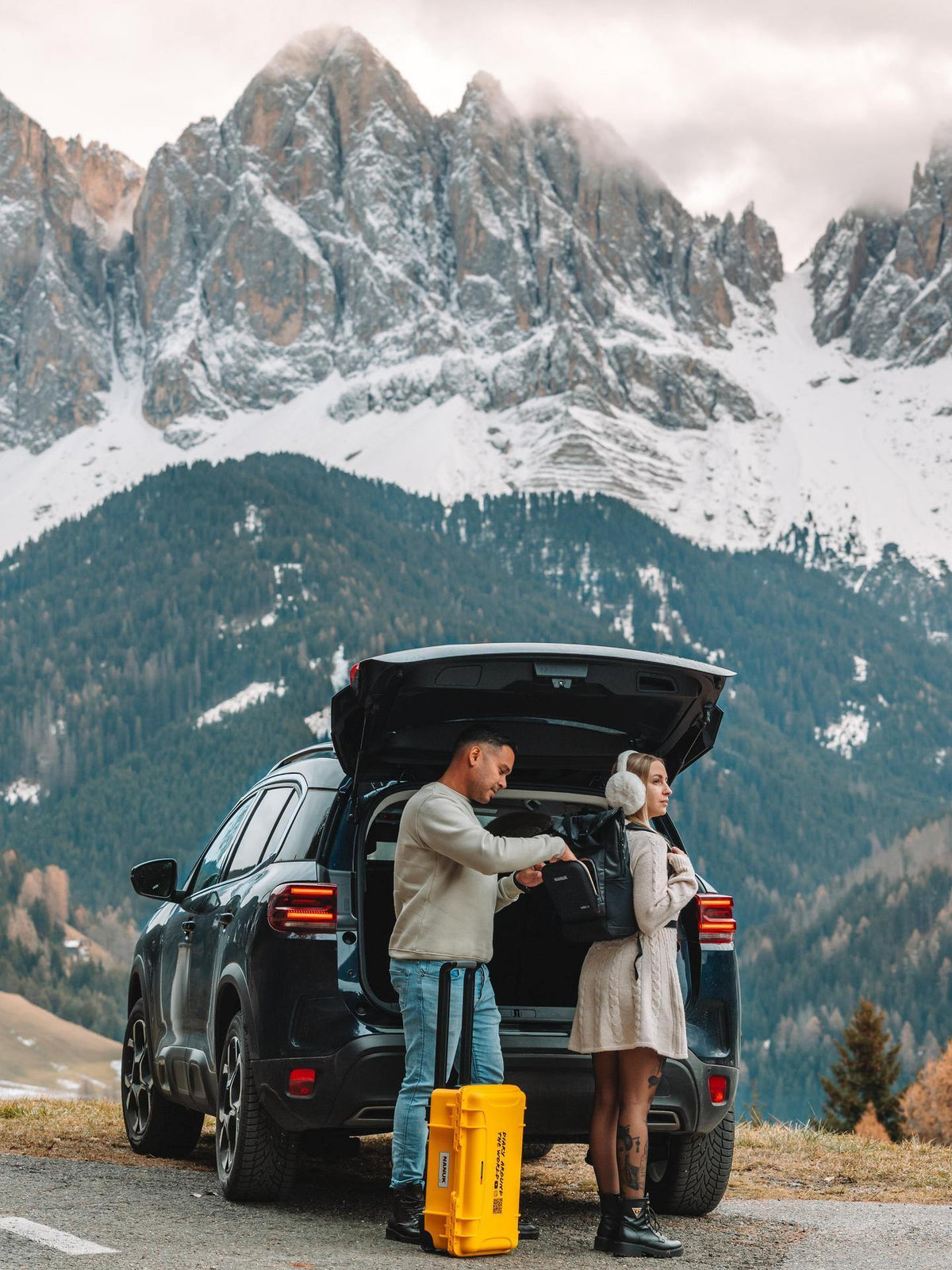Two people by an open car trunk in a mountainous area