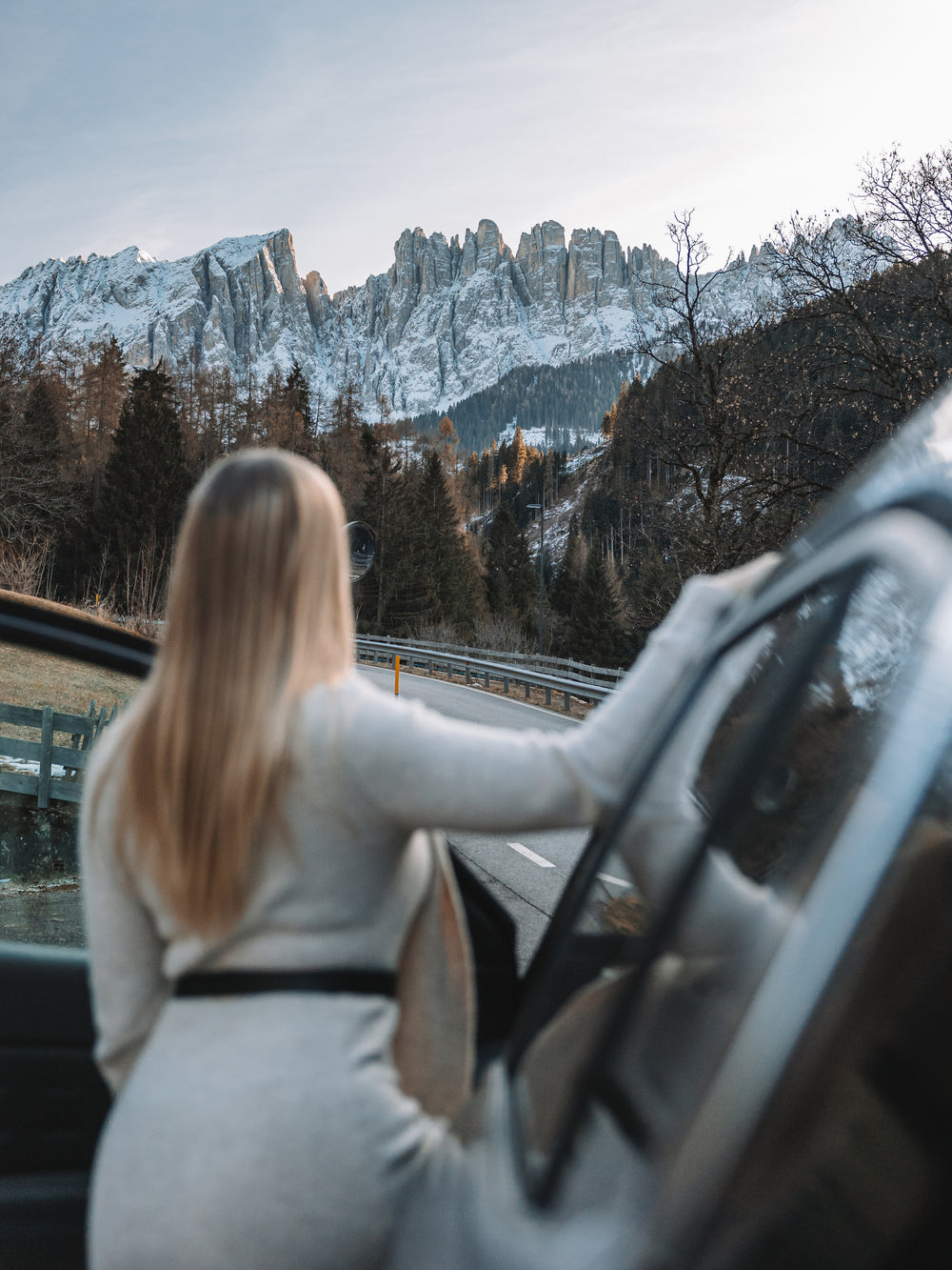 Woman sitting in a car looking at snow-capped mountains and trees.