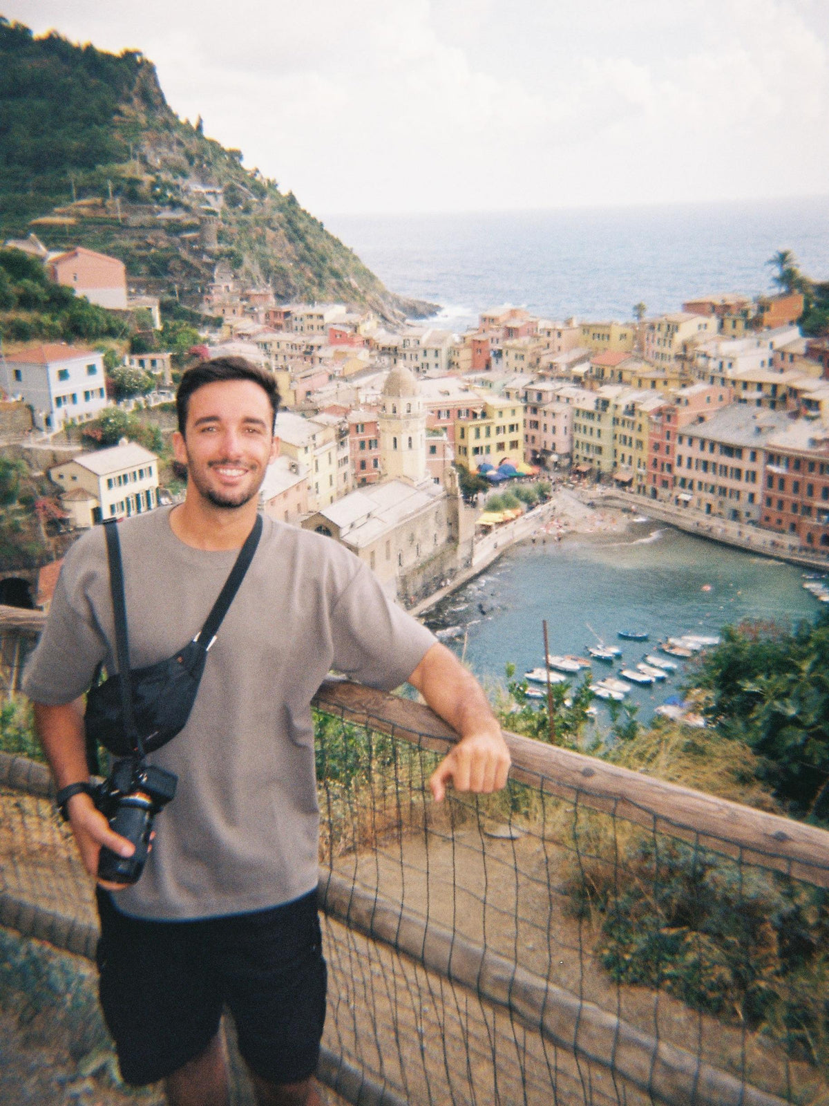 Man with a camera standing on a scenic overlook with a coastal town view.