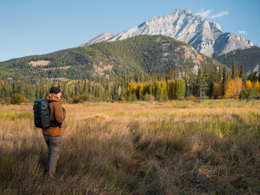 Person with a backpack standing in a field with mountains in the background