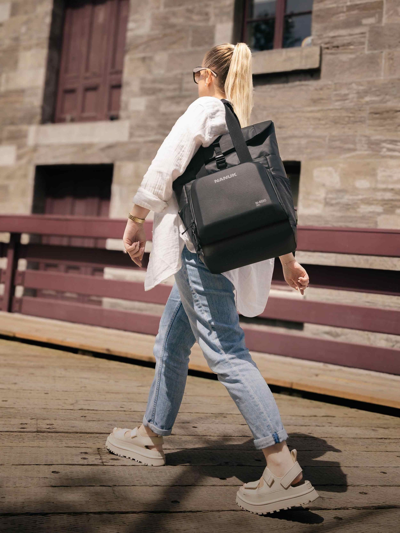 Person, die mit einer schwarzen Tasche im Freien unterwegs ist und ein weißes Hemd und Blue Jeans trägt.