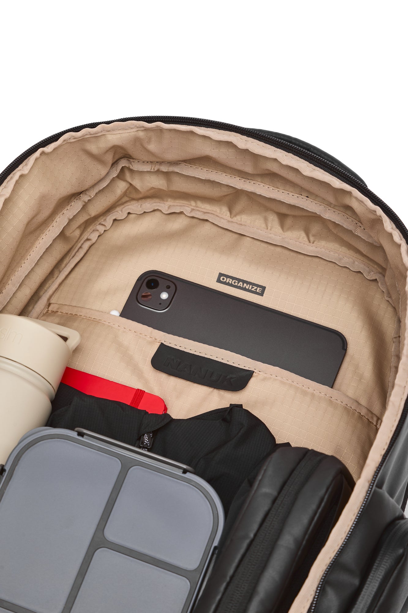 Offener Koffer mit einem Telefon, einer Wasserflasche und einer schwarzen Jacke darin auf weißem Hintergrund