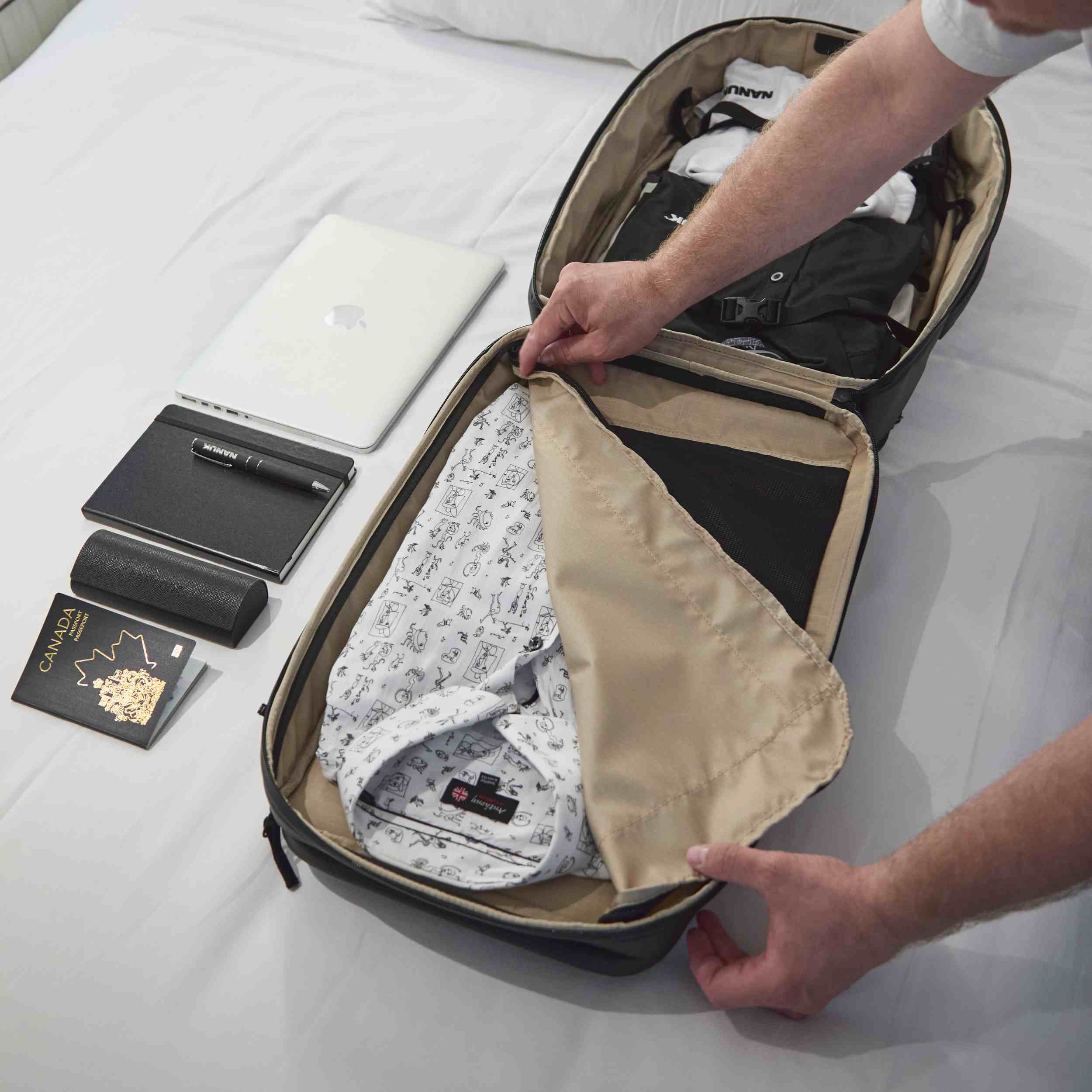 Person, die Kleidung in einen Koffer auf einem Bett packt, neben ihr liegen ein Laptop und andere Gegenstände.