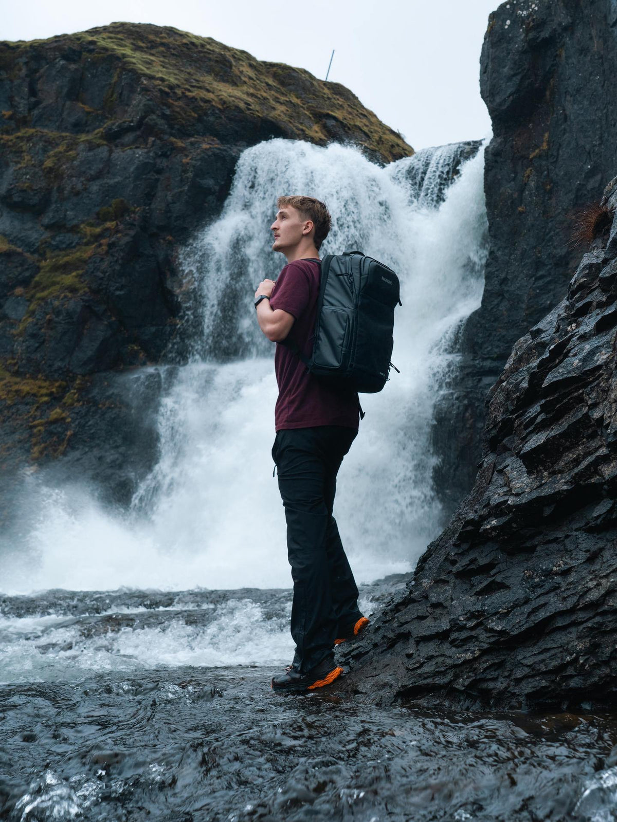 Person with a backpack standing in front of a waterfall