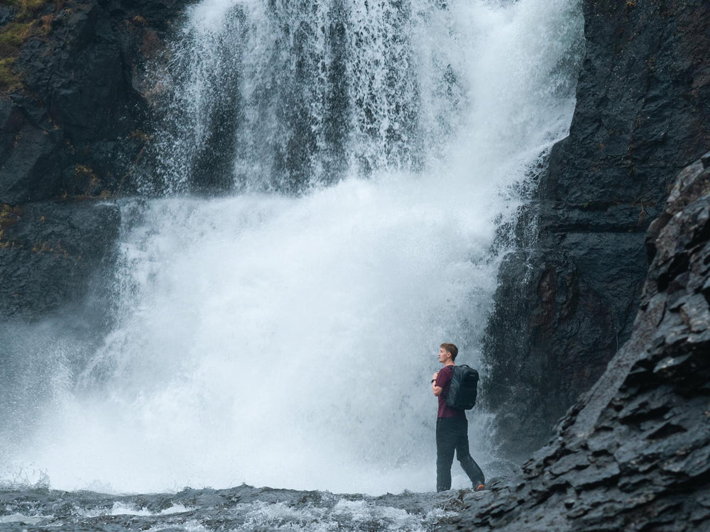 Person with a backpack standing in front of a waterfall
