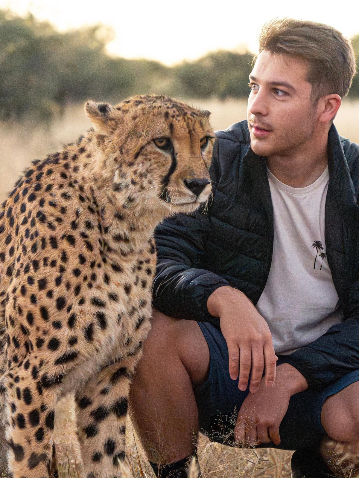 Man sitting next to a cheetah in a natural setting