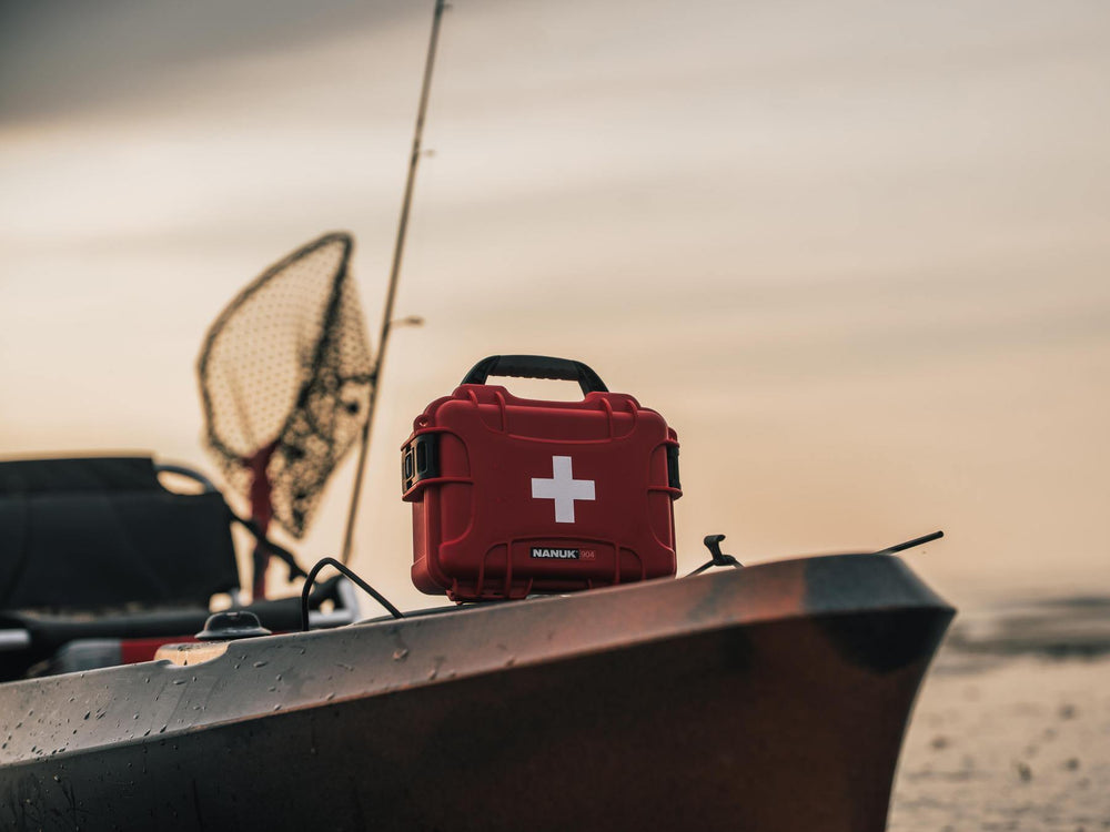 Red first aid kit with a white cross on a boat against a sunset sky.