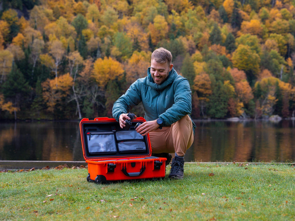 Man opening a red suitcase by a lake with trees in the background