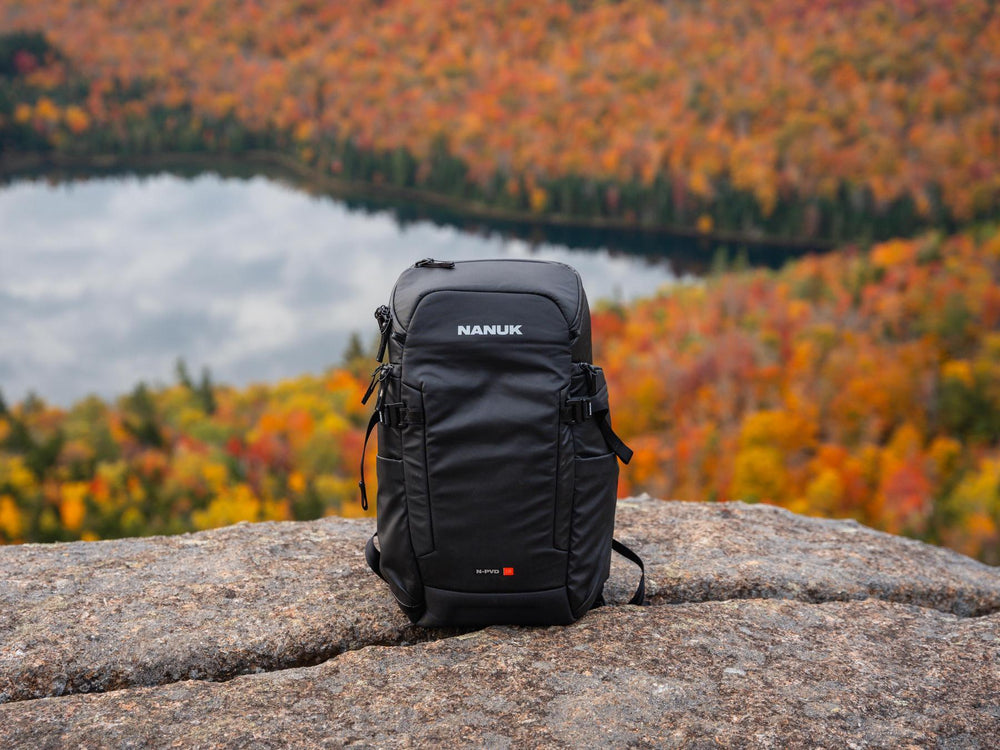 Black Nanuk backpack on a rock with a scenic autumn landscape in the background