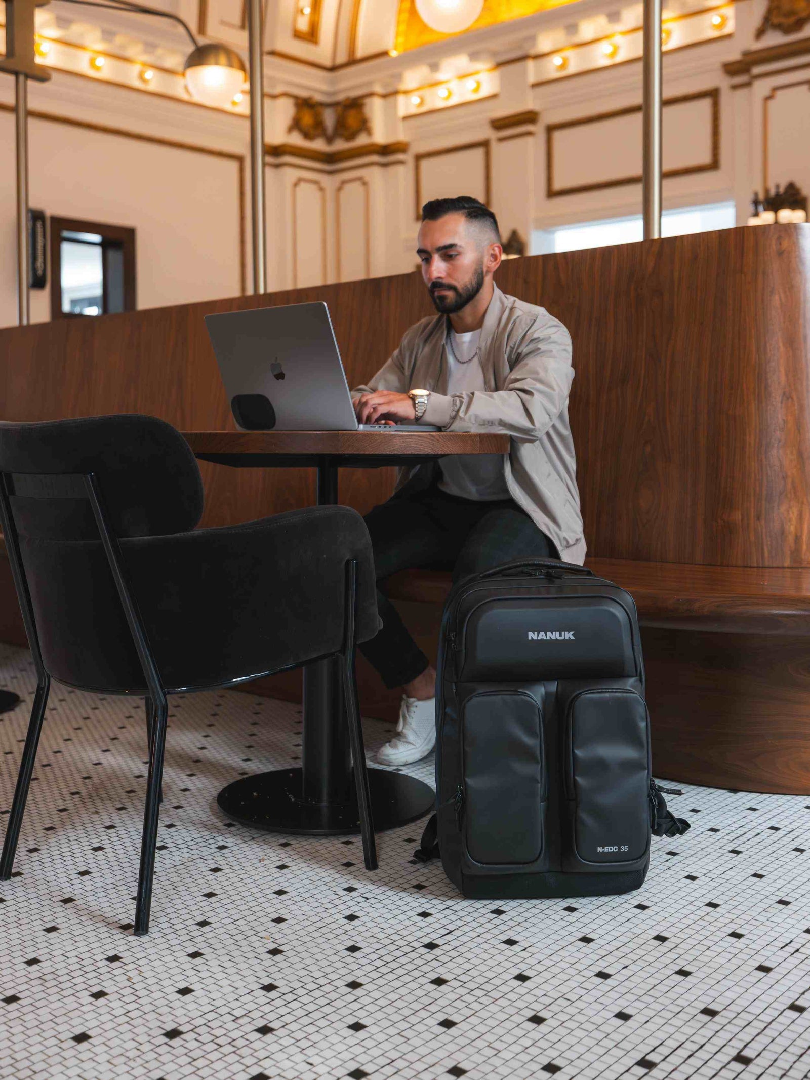 Mann, der in einem modernen Café mit einem schwarzen Rucksack auf dem Boden einen Laptop benutzt.