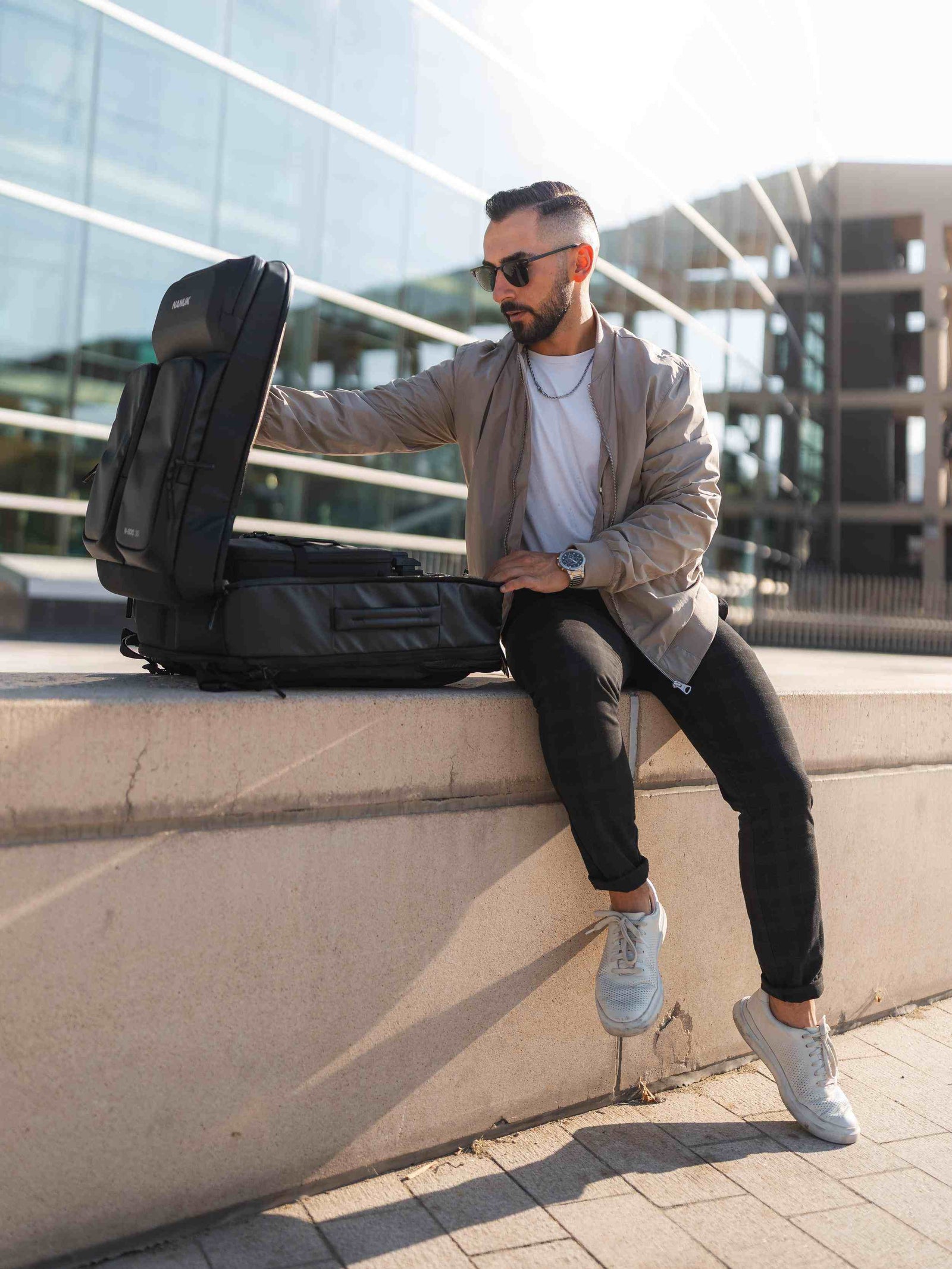 Mann sitzt mit einem großen schwarzen Rucksack auf einem Vorsprung in einer städtischen Umgebung