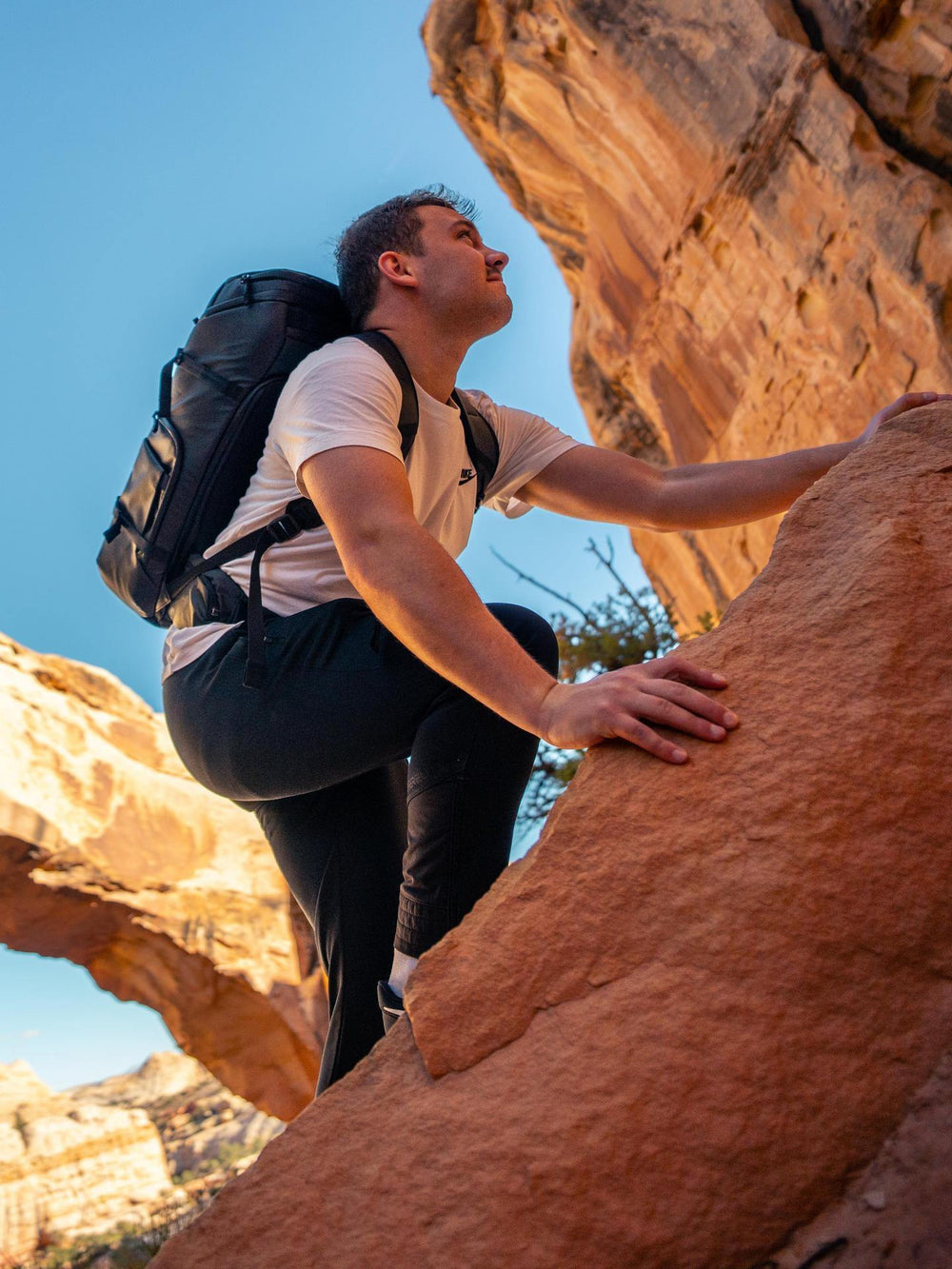 Man climbing a rock face with a backpack in a desert landscape