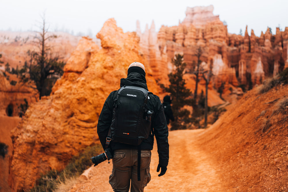 Person with a backpack walking through a desert landscape with orange rock formations.