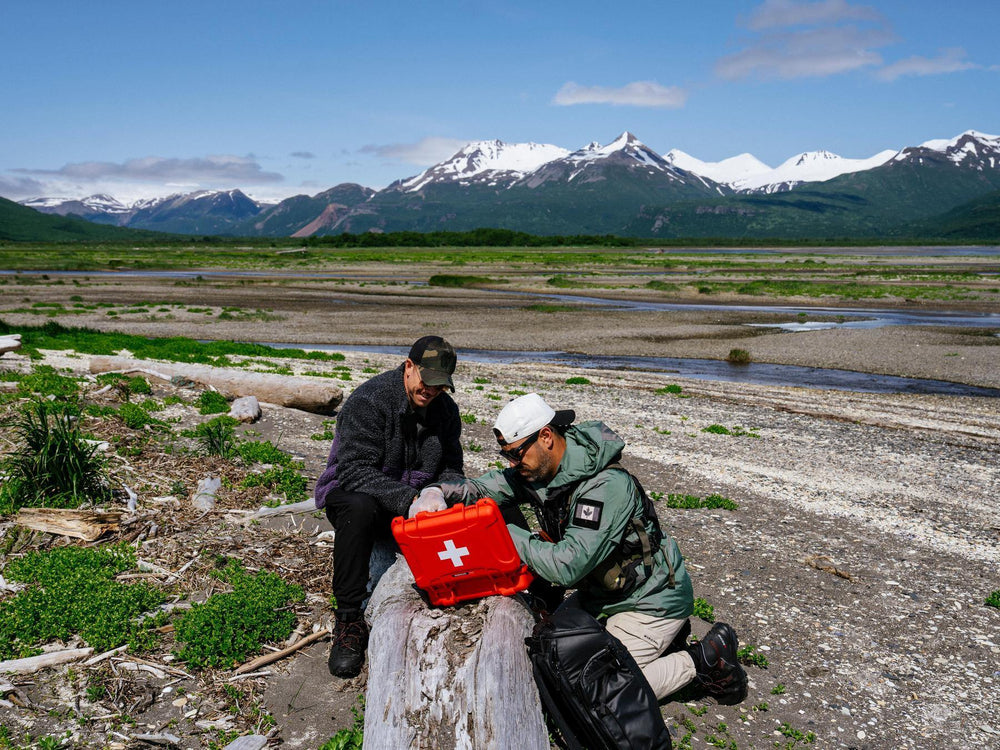 Two people with a red first aid kit in a mountainous landscape