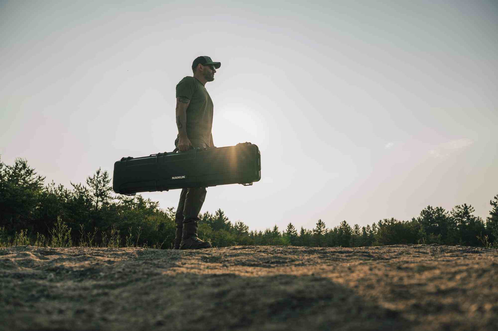 Eine Person, die einen großen schwarzen valise einem Naturhintergrund mit Bäumen und offenem Himmel hält.