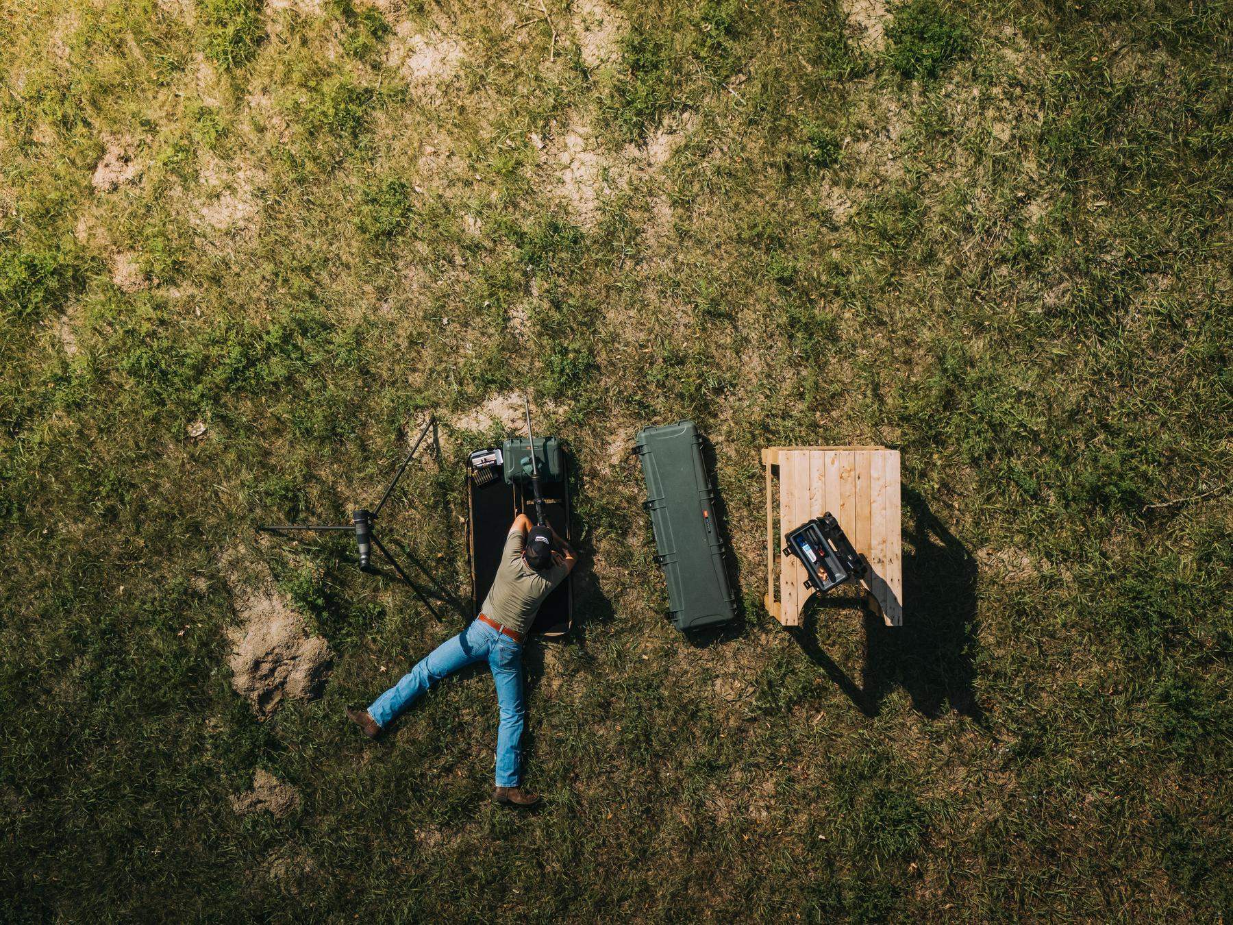 Person lying on grass next to a backpack and wooden box in an open field