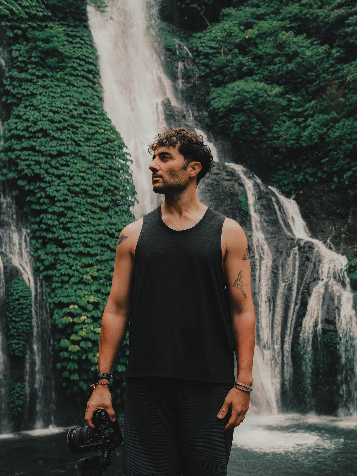 Man standing in front of a waterfall surrounded by greenery
