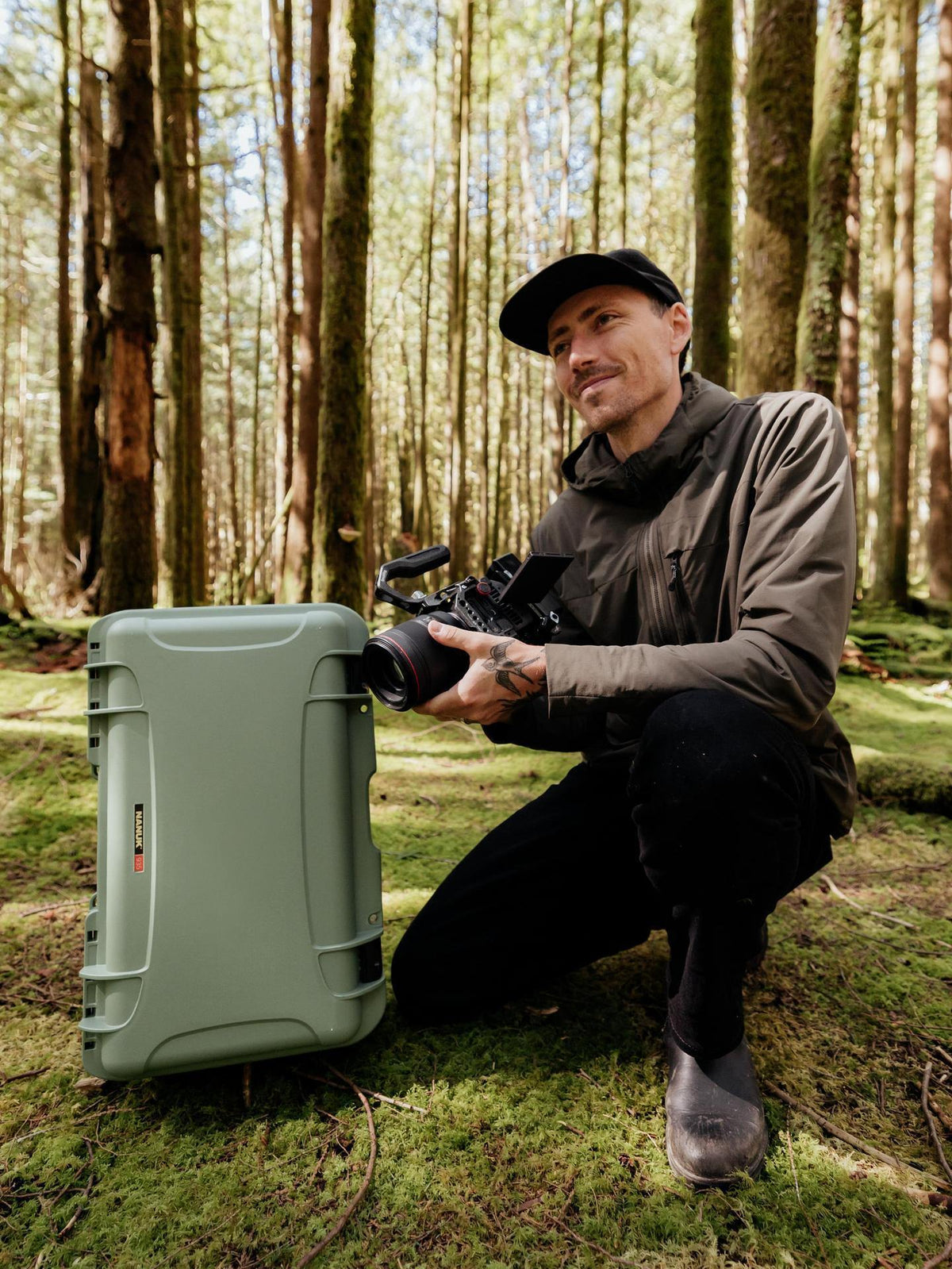 Man in a forest setting with a camera and large green case