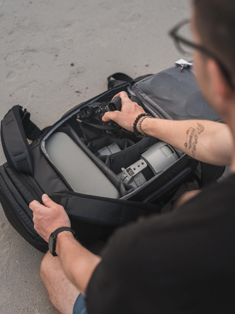 Person organizing items in a black backpack on a concrete surface