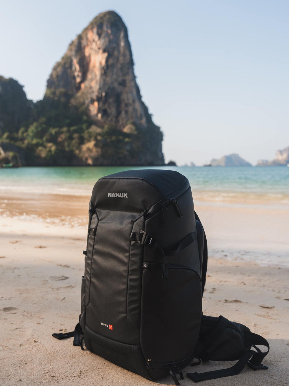 Black backpack on a beach with a mountain and ocean in the background