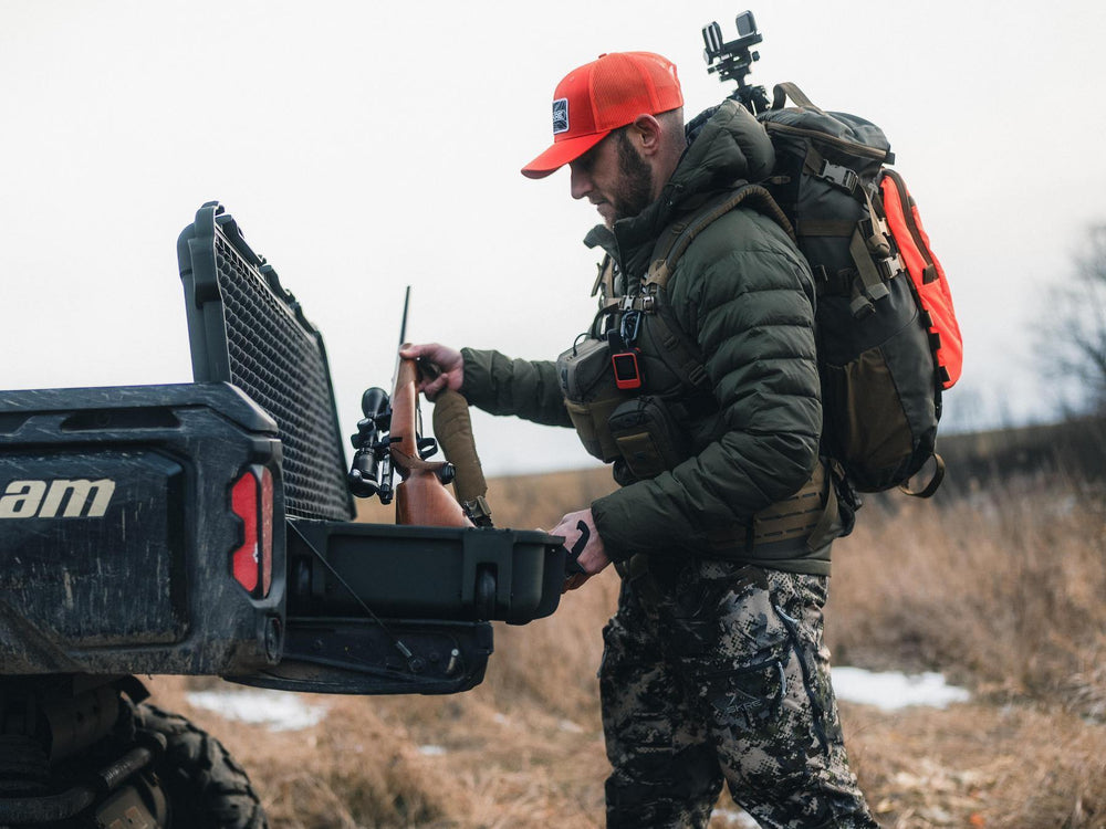 Man with hunting gear loading a bow into a truck bed.
