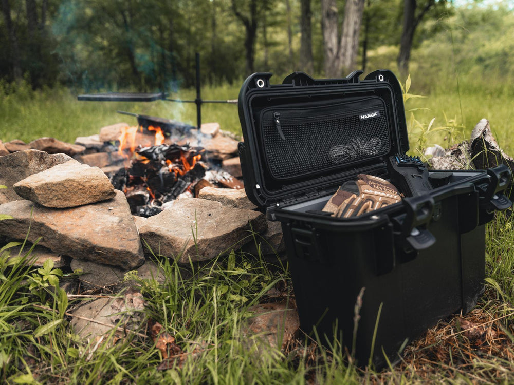 Black NANUK case next to a campfire in a forest setting
