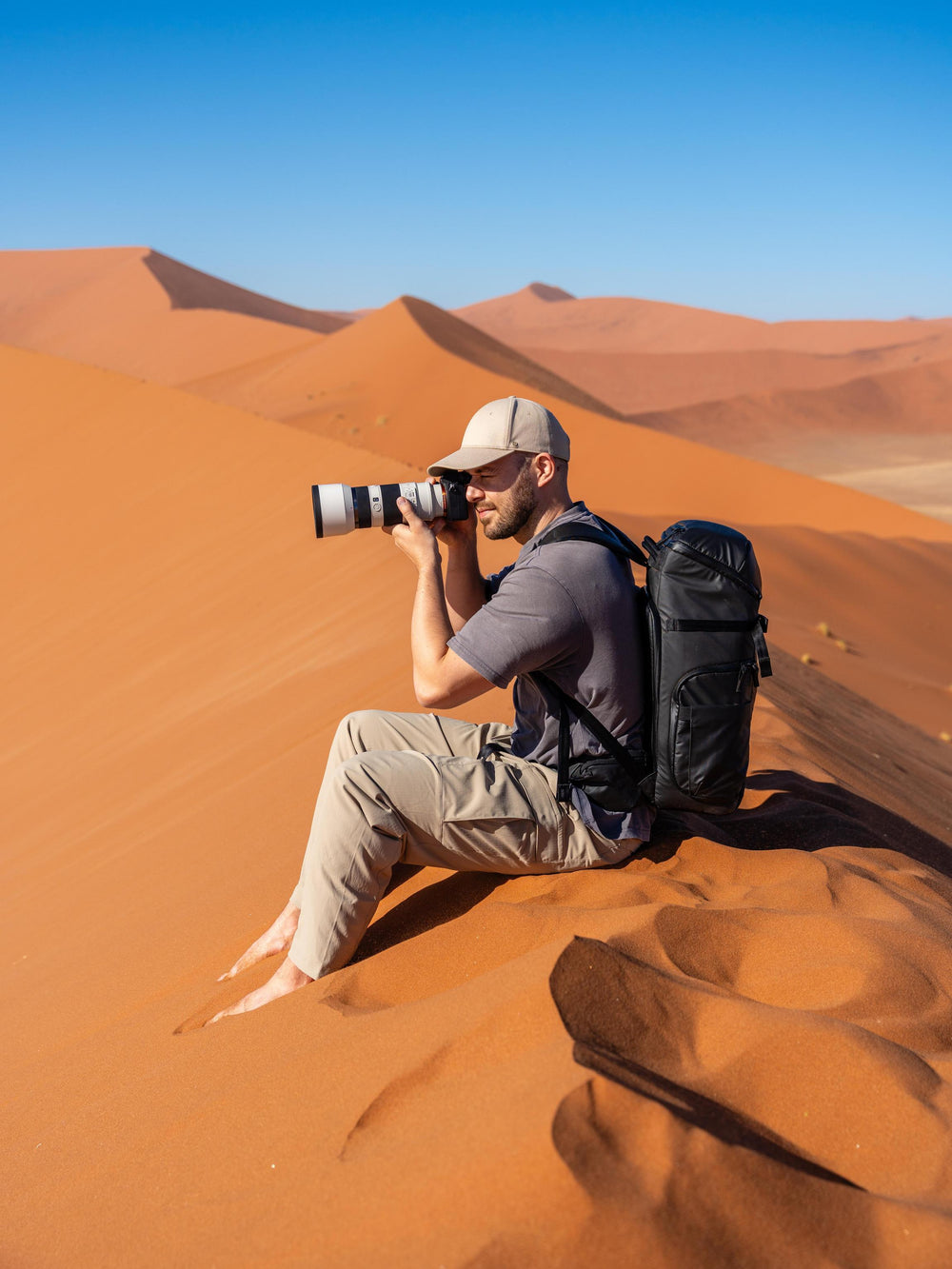 Man taking a photograph in the desert with a camera and backpack.