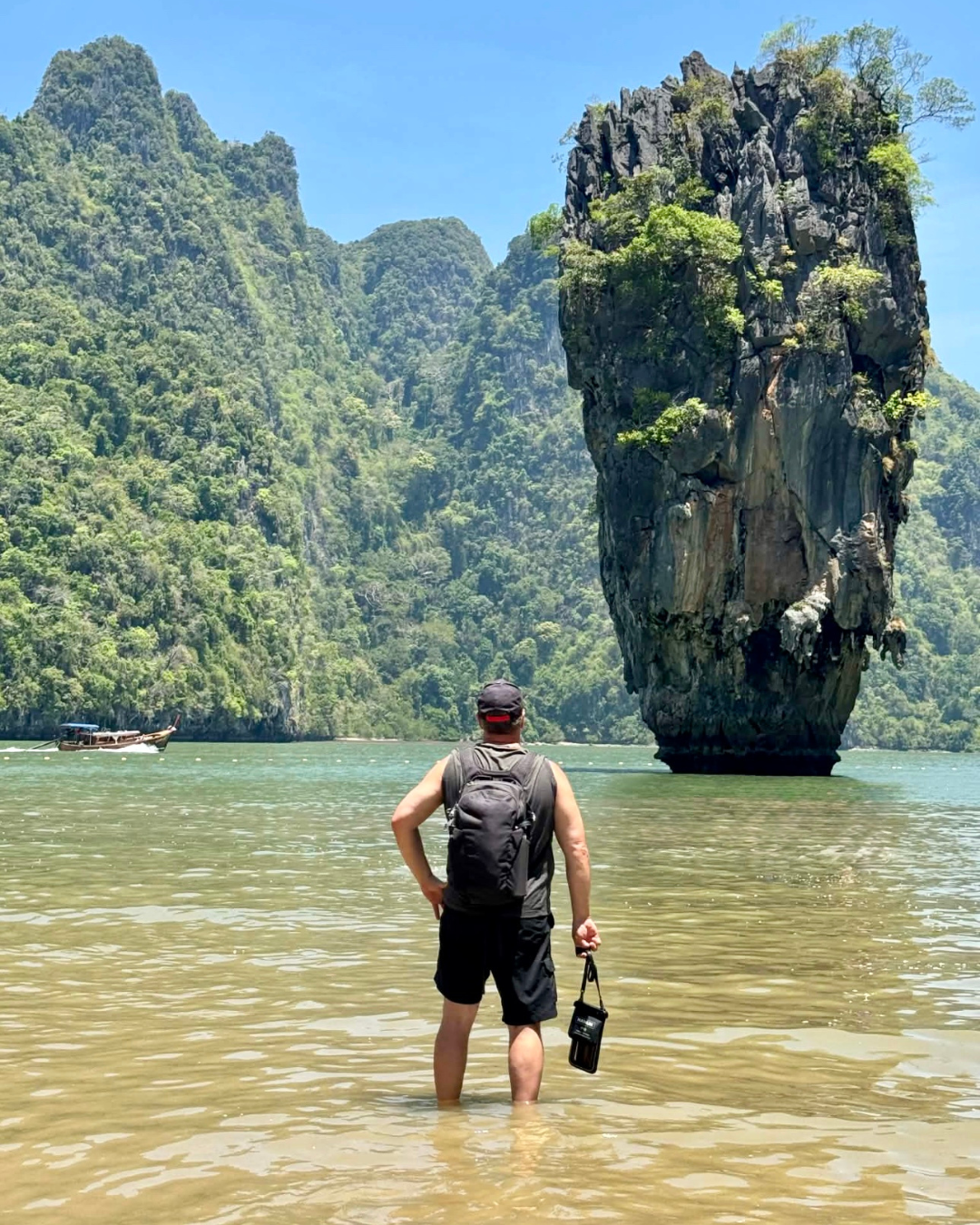 Eine Person steht im Wasser, im Hintergrund sind eine malerische Felsformation und Berge zu sehen