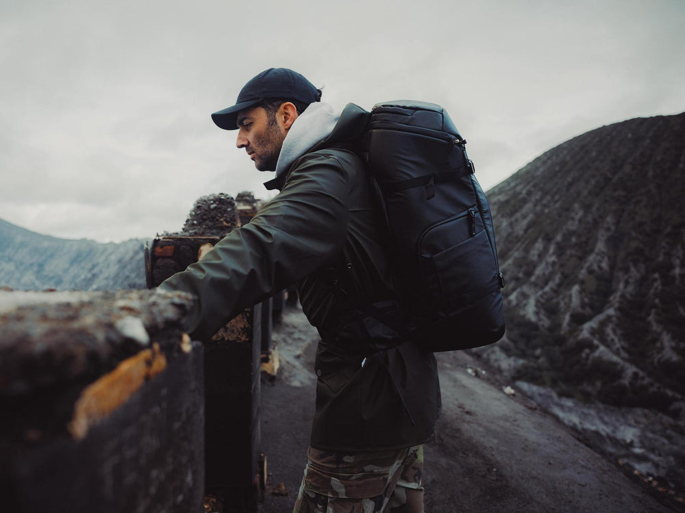 Person with a backpack standing on a mountain road with mountains in the background