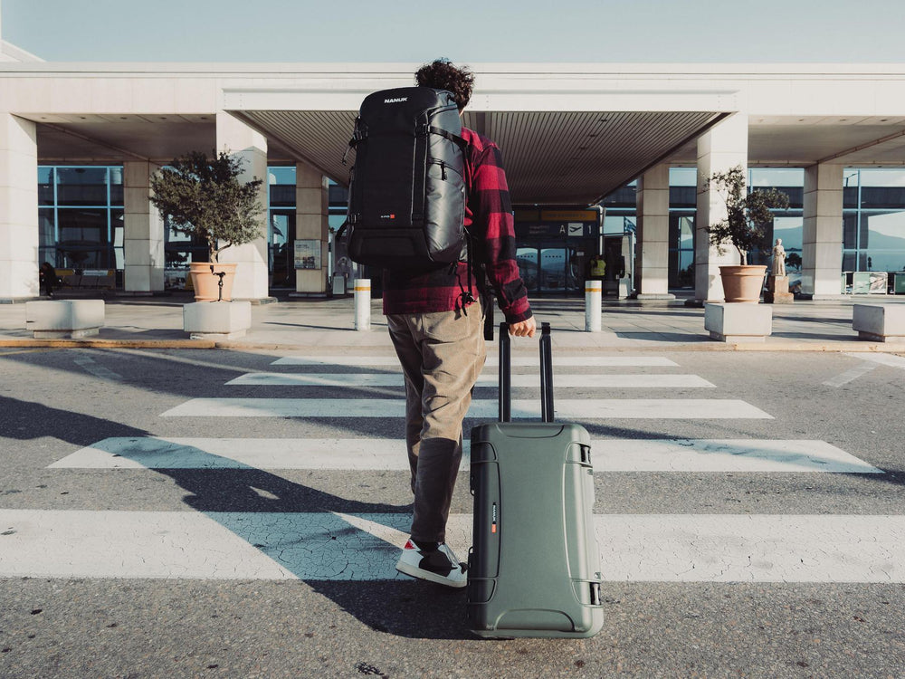 Person with a backpack and suitcase standing on a crosswalk in front of a building.