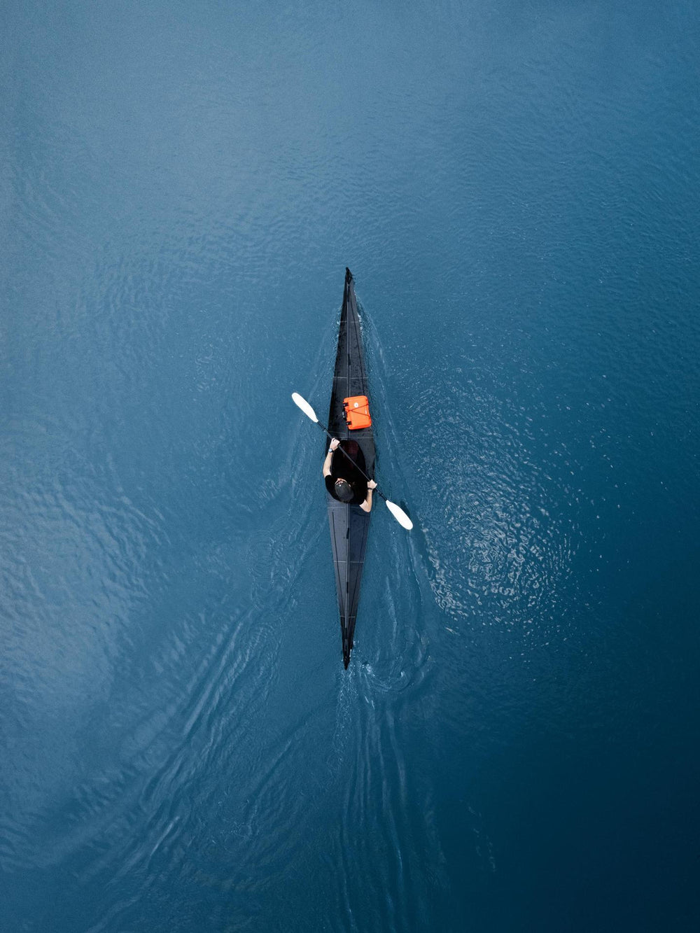 Person kayaking on a calm blue lake from an aerial perspective
