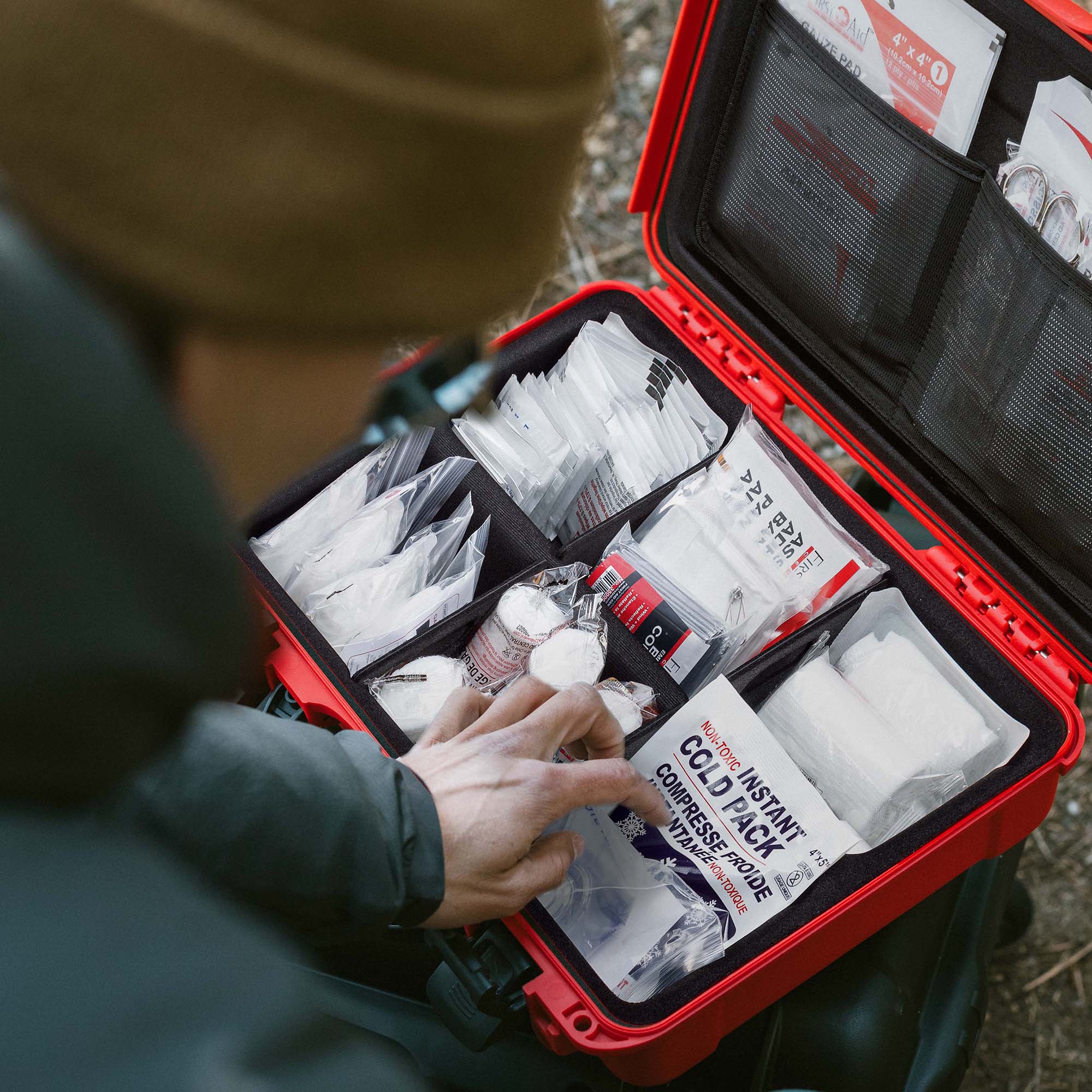 Close-up of someone arranging medical supplies inside a red NANUK First Aid Case in a wooded area.