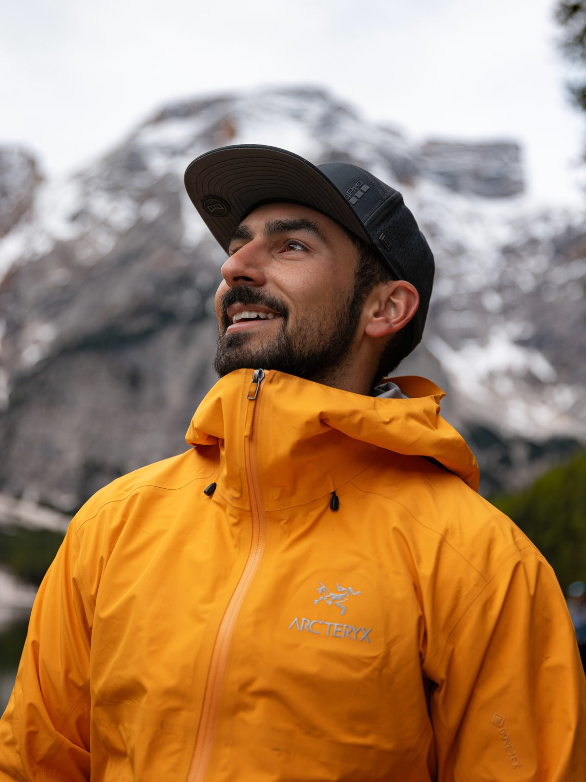 Man wearing a yellow jacket with a brand logo against a mountainous background